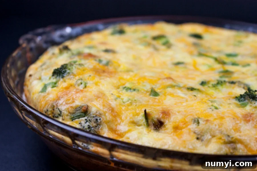 A round glass pie dish filled with the crustless broccoli and cheddar quiche mixture, ready to be baked in the oven.