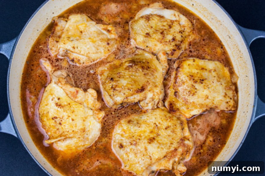 Spanish Chicken thighs seared in skillet with rice and broth added.