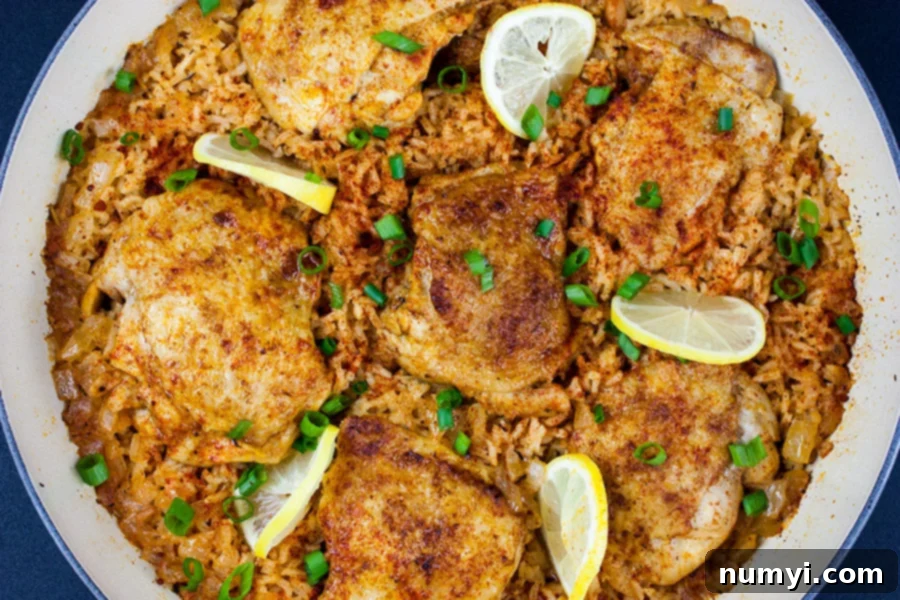 One Pan Spanish chicken and rice cooked in the skillet garnished with lemons slices and green onions.