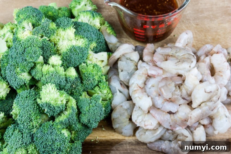 Ingredients for Shrimp and Broccoli Stir Fry: raw peeled shrimp, chopped broccoli florets, and a bowl of prepared stir fry sauce.