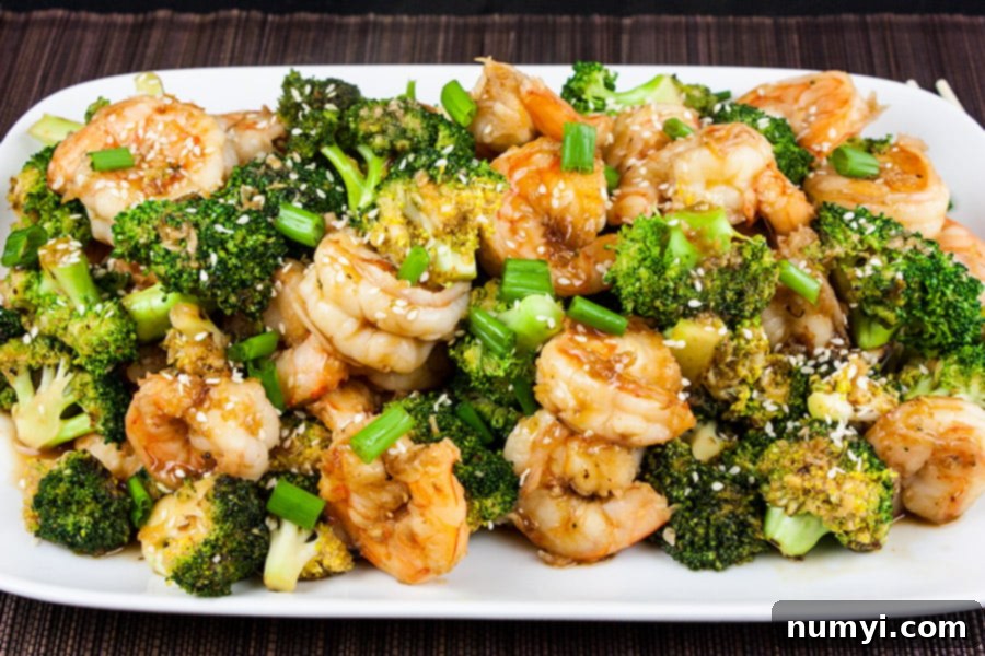 Close-up of cooked Shrimp and Broccoli Stir Fry served on a white platter, garnished with sesame seeds and chopped green onions.