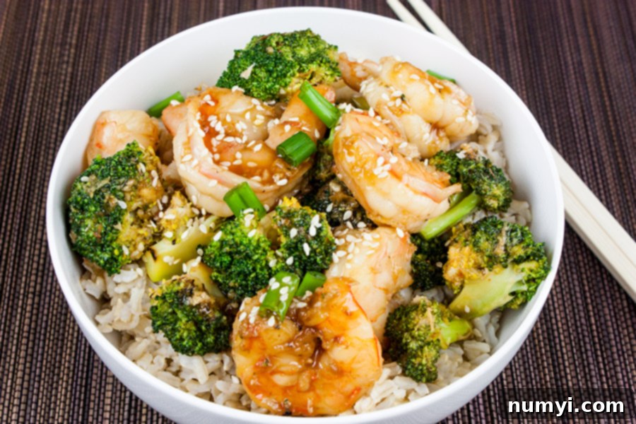 A serving of Shrimp and Broccoli Stir Fry in a white bowl, ready to be eaten with chopsticks.