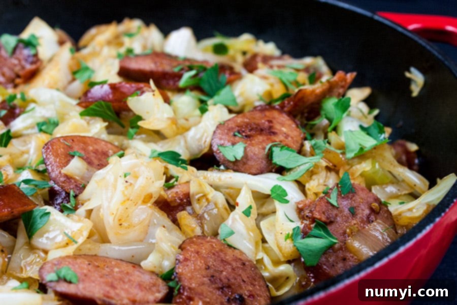 A vibrant close-up of fried cabbage and sausage sizzling in a cast-iron skillet, ready to be served.