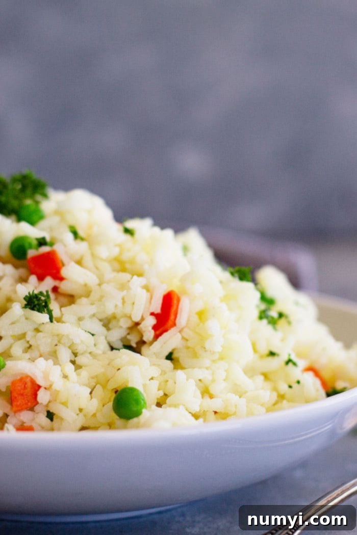 A close-up side view of fluffy rice pilaf with visible carrots and peas, showcasing its perfect texture.