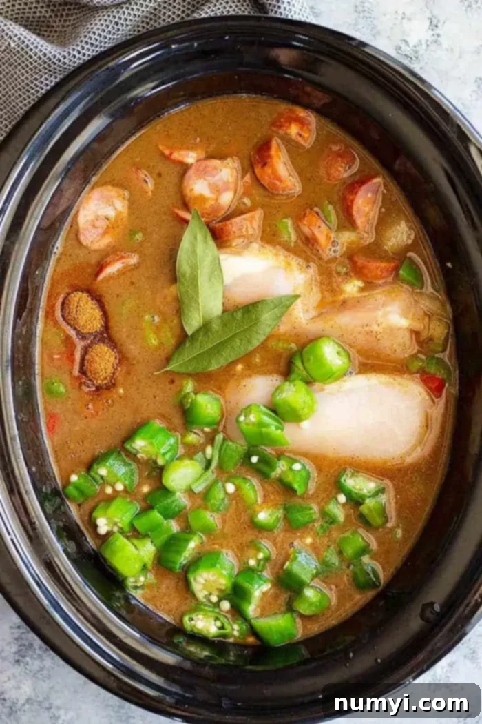 A slow cooker filled with simmering chicken, shrimp, and sausage gumbo, showing the rich, dark broth and various ingredients.