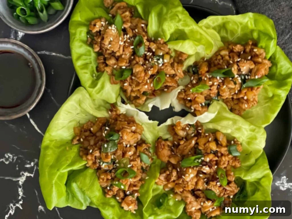 A collection of perfectly assembled chicken lettuce wraps, garnished with fresh green onions and sesame seeds, presented on an elegant dark plate.