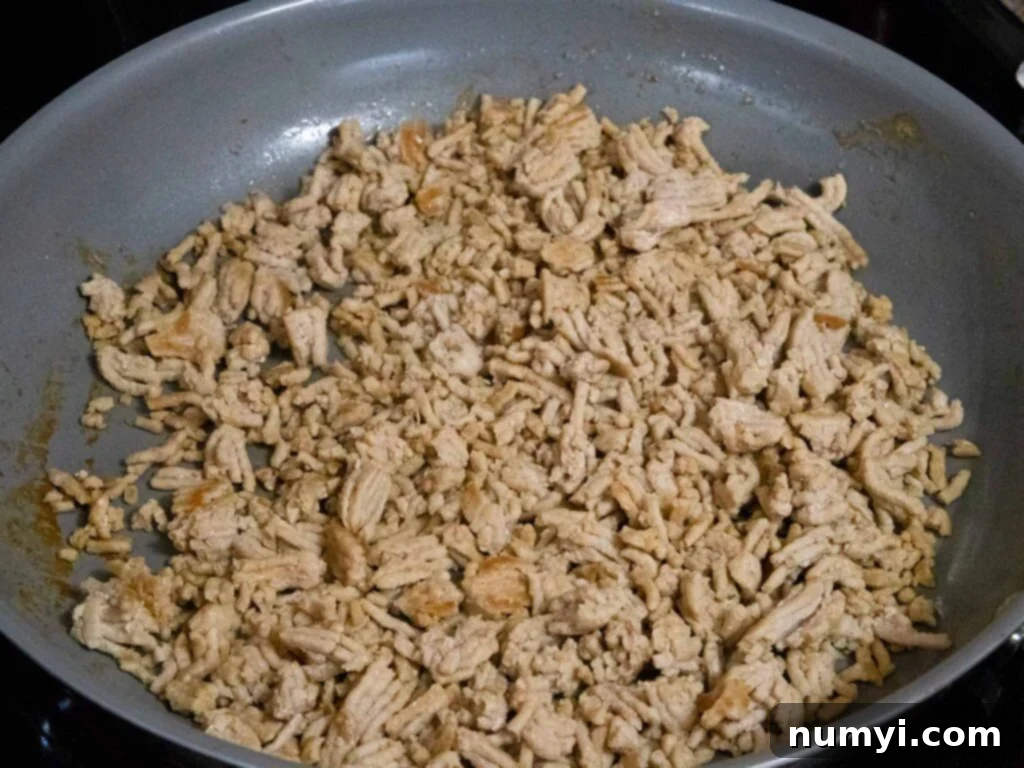Perfectly cooked and crumbled ground chicken in a skillet, showcasing its rich brown color, ready for the next step of adding aromatic flavors.