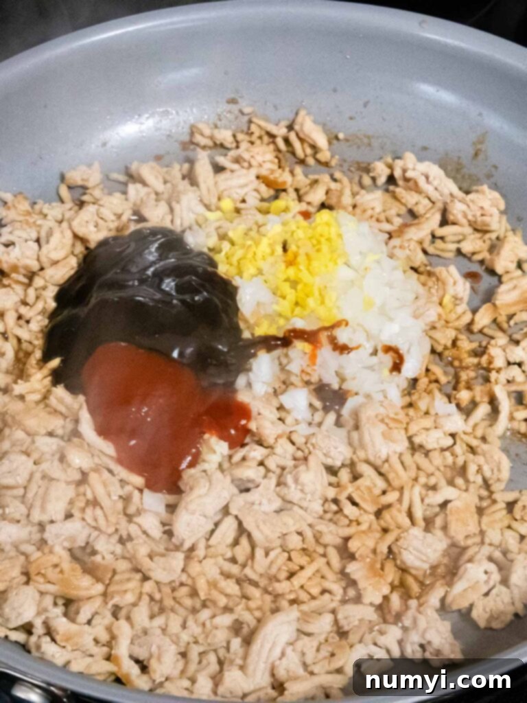 Various vibrant Asian spices and savory sauces being expertly added to the cooked ground chicken in a hot skillet, ready to infuse rich flavor.