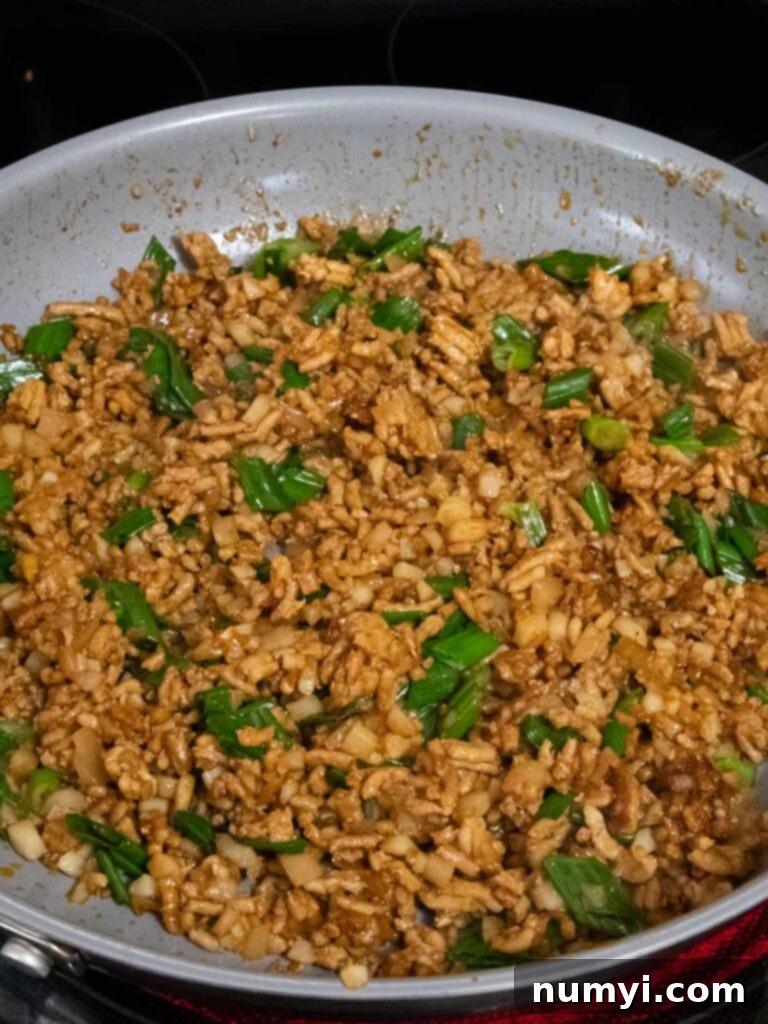 The finished filling for chicken lettuce wraps, a savory and aromatic blend with visible green onions and water chestnuts, ready to be served hot from the skillet.