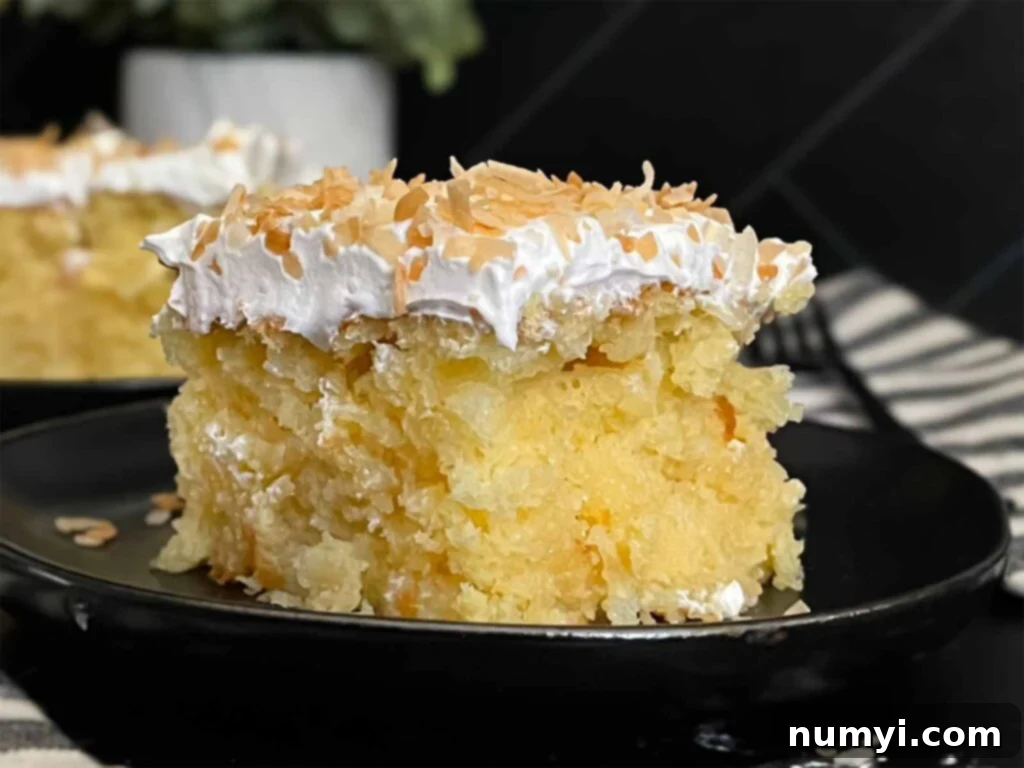 A perfectly sliced piece of moist coconut sheet cake, showcasing its delicate texture and creamy topping, resting on a dark plate against a complementary dark surface.
