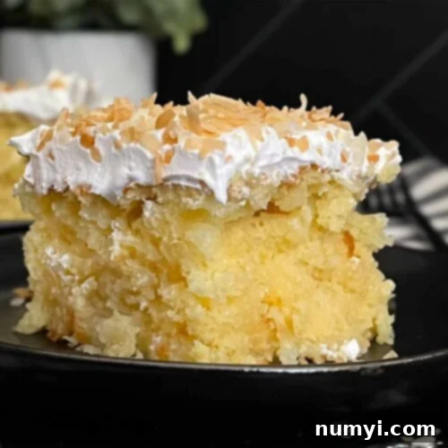 A slice of our Easy Coconut Sheet Cake, incredibly moist and topped with shredded coconut, on a dark plate ready to enjoy.