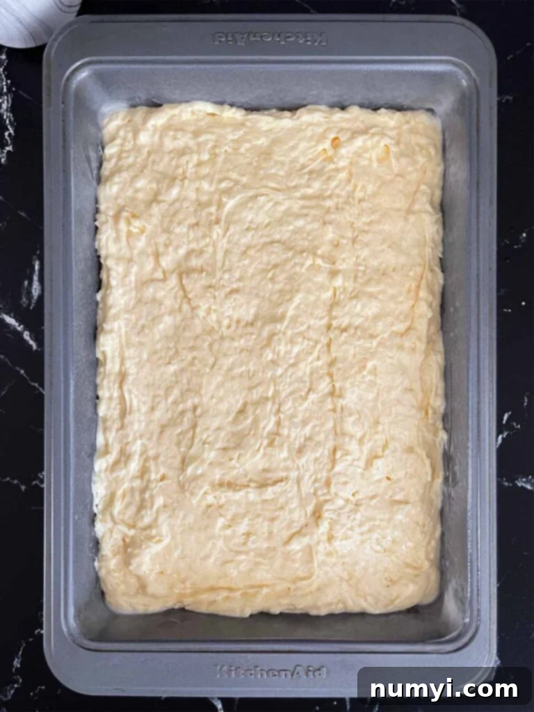 Coconut sheet cake batter smoothly spread into a 9x13 baking pan, ready for the oven.