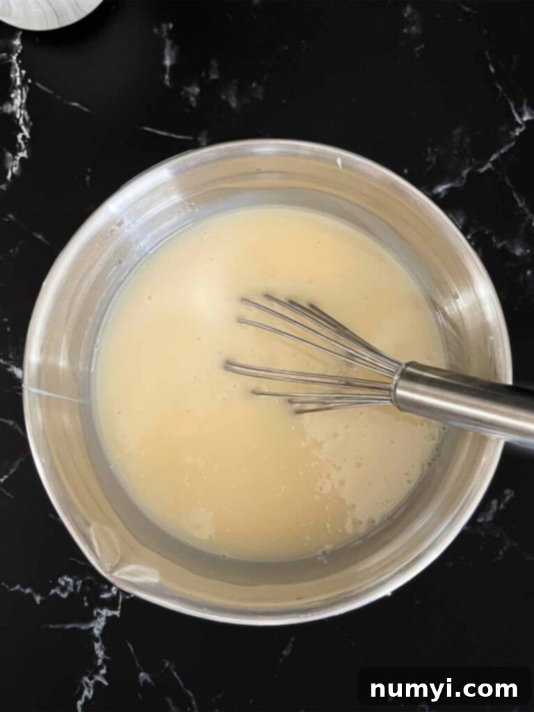 Smooth, combined cream of coconut and sweetened condensed milk mixture in a metal mixing bowl on a dark surface.