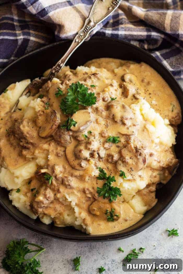 Closeup overhead shot of hamburger stroganoff recipe over mashed potatoes in a black bowl, showing the rich, creamy sauce and tender mushrooms.