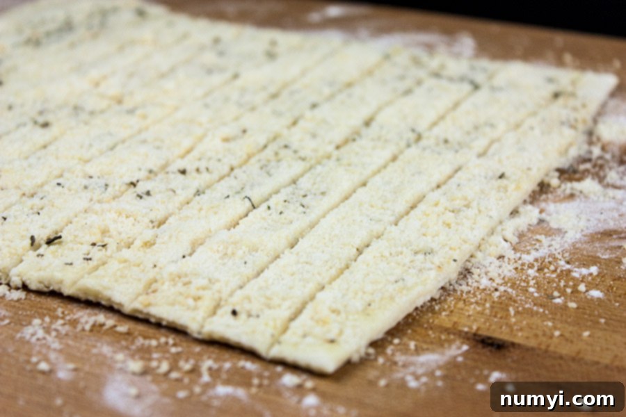 Puff pastry dough rolled out on a cutting board, generously sprinkled with grated Parmesan and Gruyere cheese and Italian herbs.