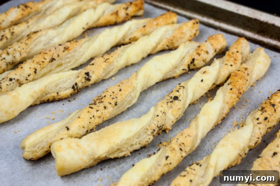 Freshly baked golden brown cheese straws on a baking sheet, hot from the oven.