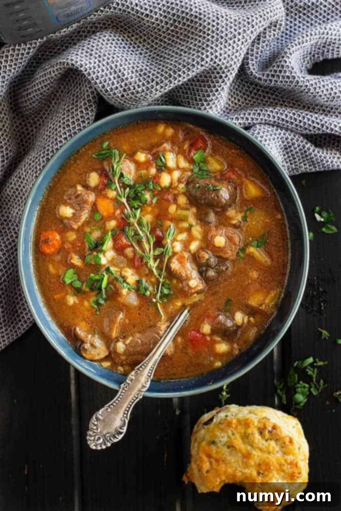 overhead: instapot beef barley soup in a blue bowl served with fresh biscuits