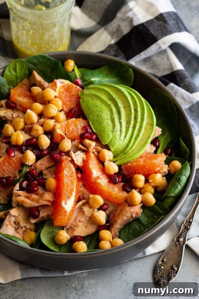 A large bowl of vibrant spinach salad with flaky salmon and creamy avocado, generously sprinkled with freshly ground black pepper.
