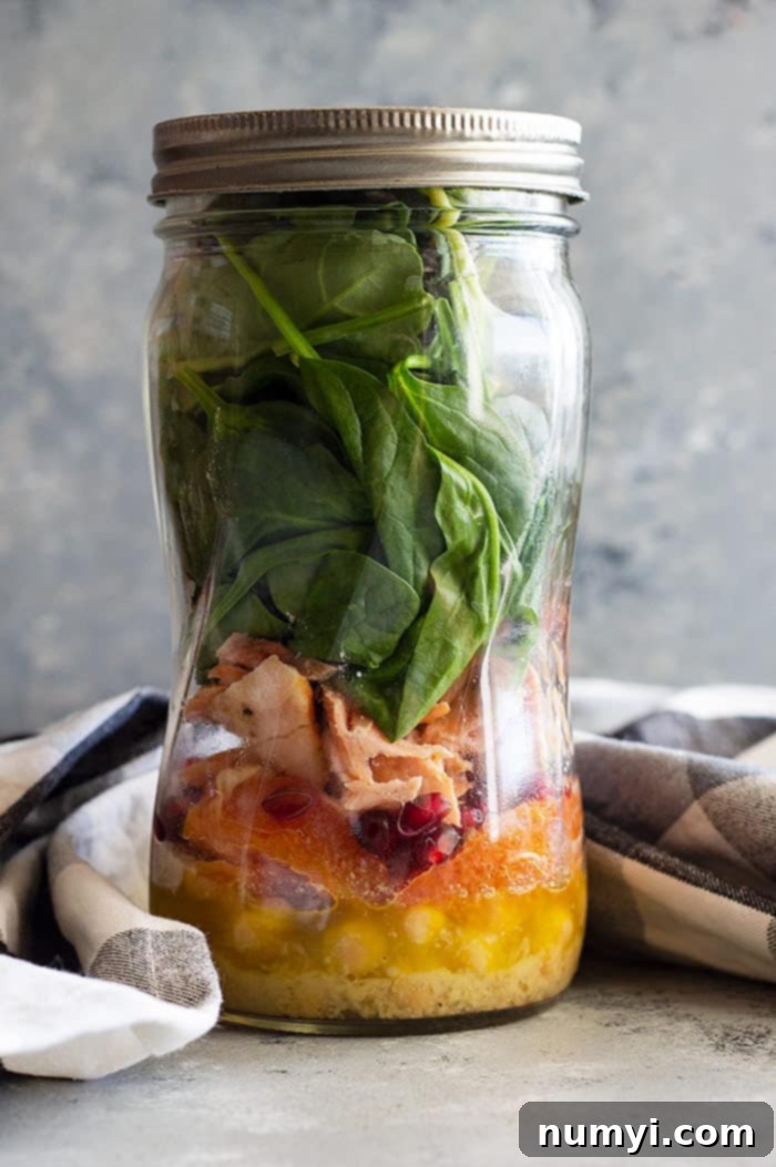 Spinach salad with salmon and avocado beautifully arranged in a mason jar for convenient meal prep, showing layers of ingredients.