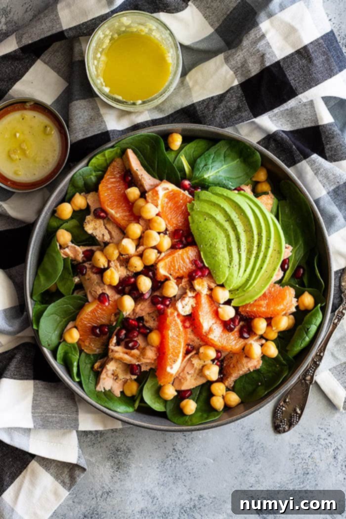 Top-down view of a beautifully arranged spinach salad with salmon and avocado, accompanied by a small bowl of dressing on the side.