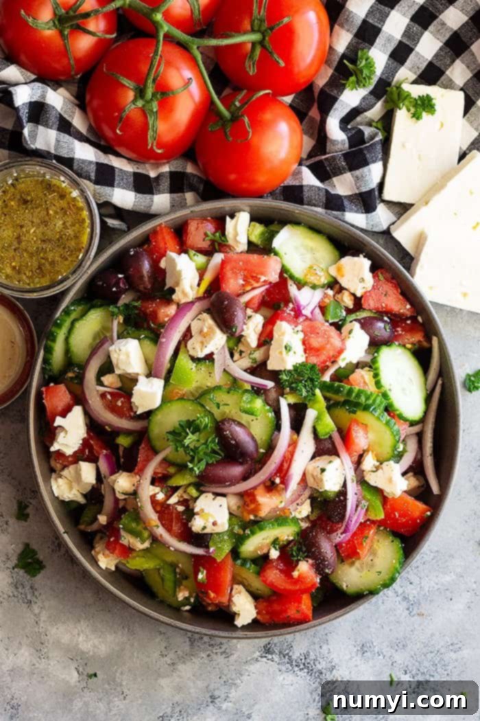 Top down view of a large bowl of Easy Greek Salad, brimming with fresh, colorful vegetables like juicy red tomatoes, crisp green cucumbers, vibrant green bell peppers, deep purple Kalamata olives, and crumbled white feta cheese.