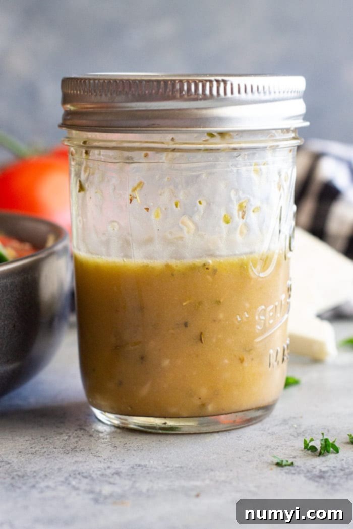 A mason jar filled with homemade Greek Salad dressing, showcasing the rich olive oil, red wine vinegar, and herbs, ready to be shaken and drizzled over fresh vegetables.