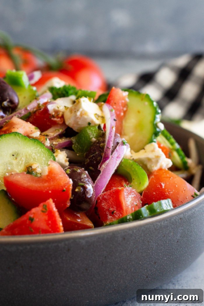 A close up view of a serving of Easy Greek Salad, highlighting the texture of the feta cheese, the glossy olives, and the vibrant colors of the freshly chopped vegetables, coated in a light dressing.
