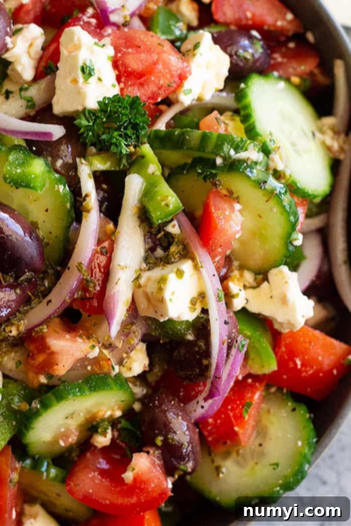 A top down view of a vibrant and healthy Easy Greek Salad, ready to be served. The colors of the fresh vegetables are enhanced by a light drizzle of homemade dressing, with a focus on the abundant feta and olives.