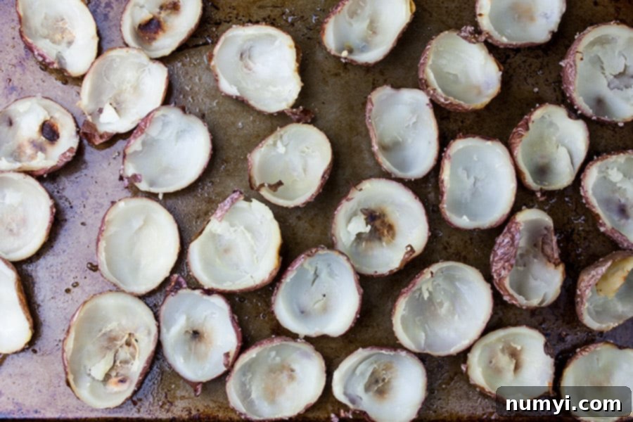 Small red potato skins, hollowed out and ready for a second bake on a baking sheet, forming the base for Deviled Potato Bites.