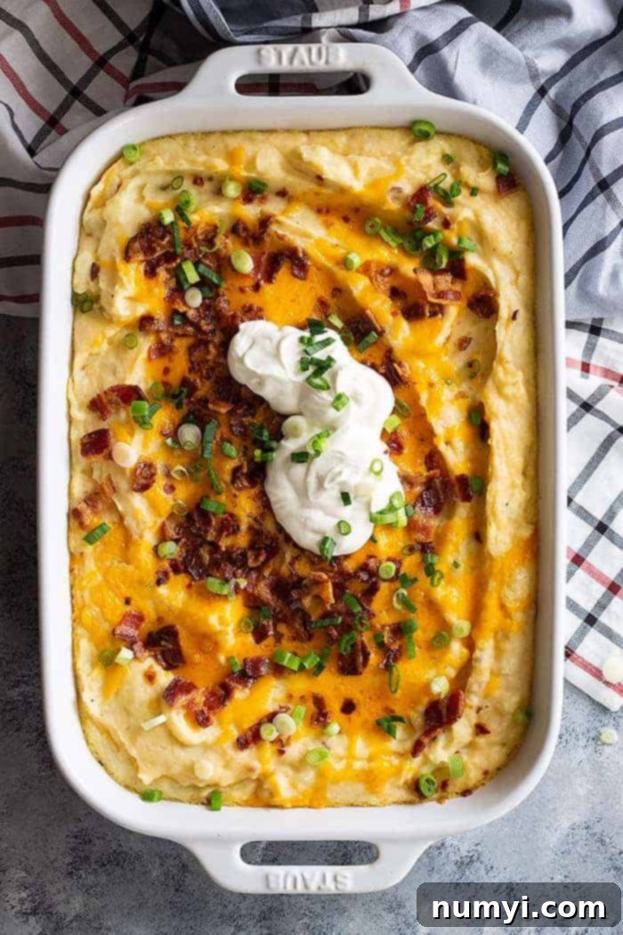 overhead: loaded mashed potato casserole in a whit staub dish with cheese, bacon, and sour cream on top, ready to serve