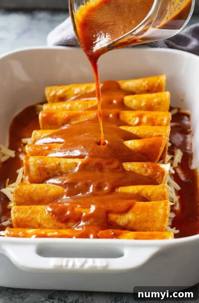 A close-up of vibrant red enchilada sauce being generously poured over a pan of freshly assembled cheese enchiladas before baking, promising rich flavor.