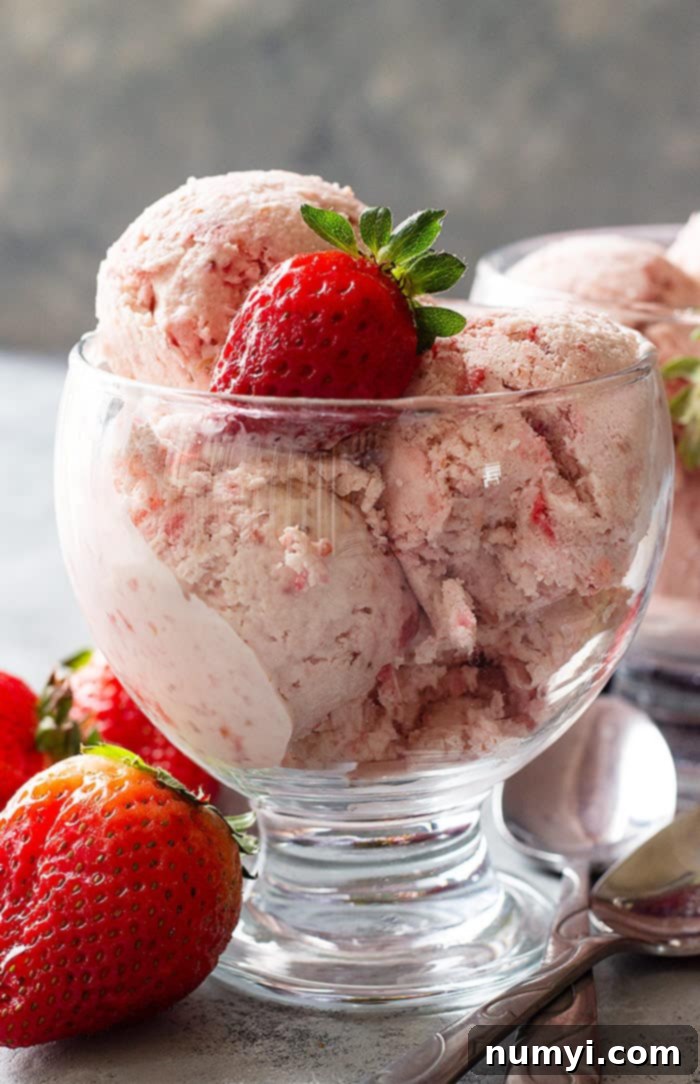 A beautiful dessert cup filled with generous scoops of creamy strawberry ice cream, perfectly topped with a fresh, ripe strawberry, ready to be enjoyed.