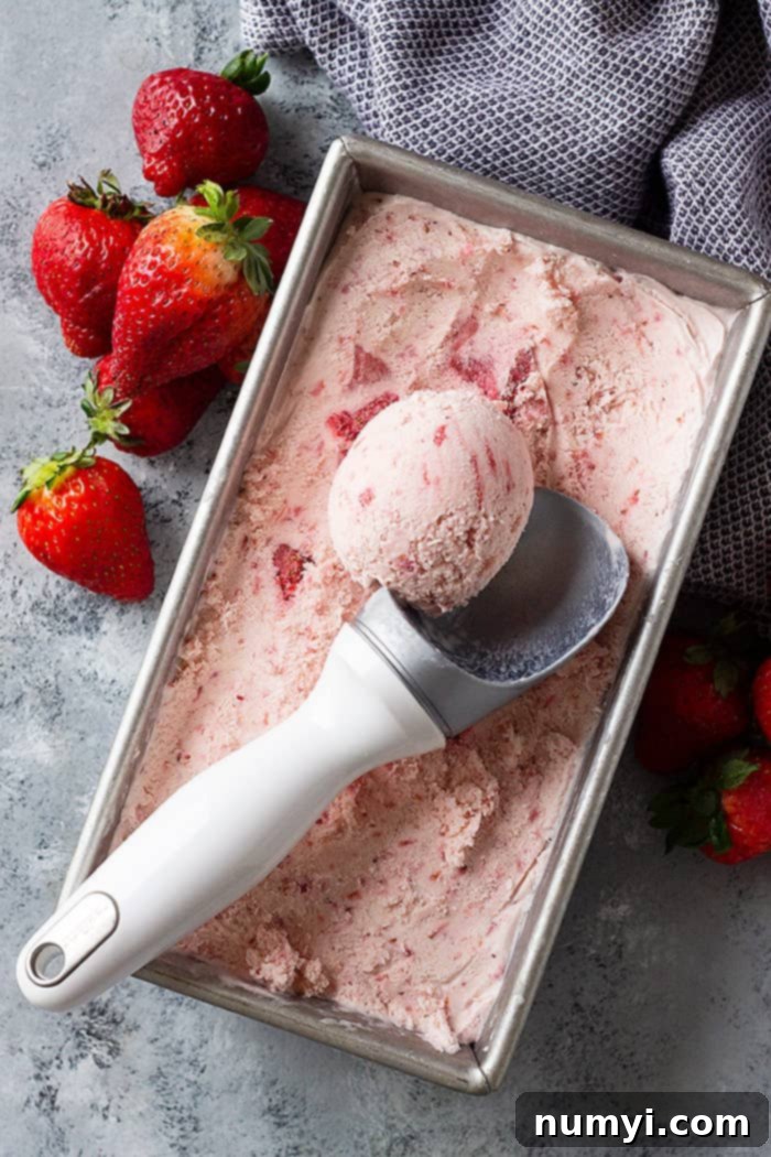 A top-down view of a pan filled with freshly made no-churn strawberry ice cream, with a scoop being taken out, revealing its smooth and inviting texture.