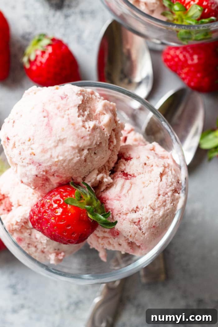 A captivating top-down view of scoops of creamy strawberry ice cream elegantly presented in a bowl, garnished with a fresh strawberry, highlighting its delicious appeal.