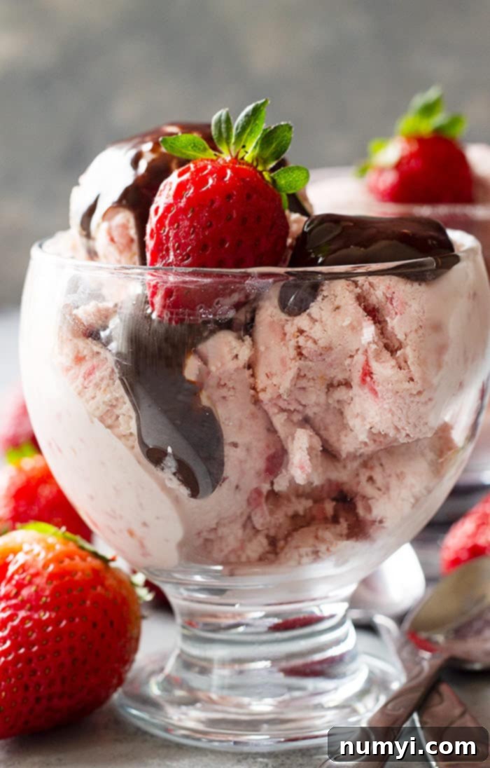 A dessert cup generously filled with luscious strawberry ice cream, drizzled with rich hot fudge sauce and crowned with a fresh strawberry, creating an enticing treat.