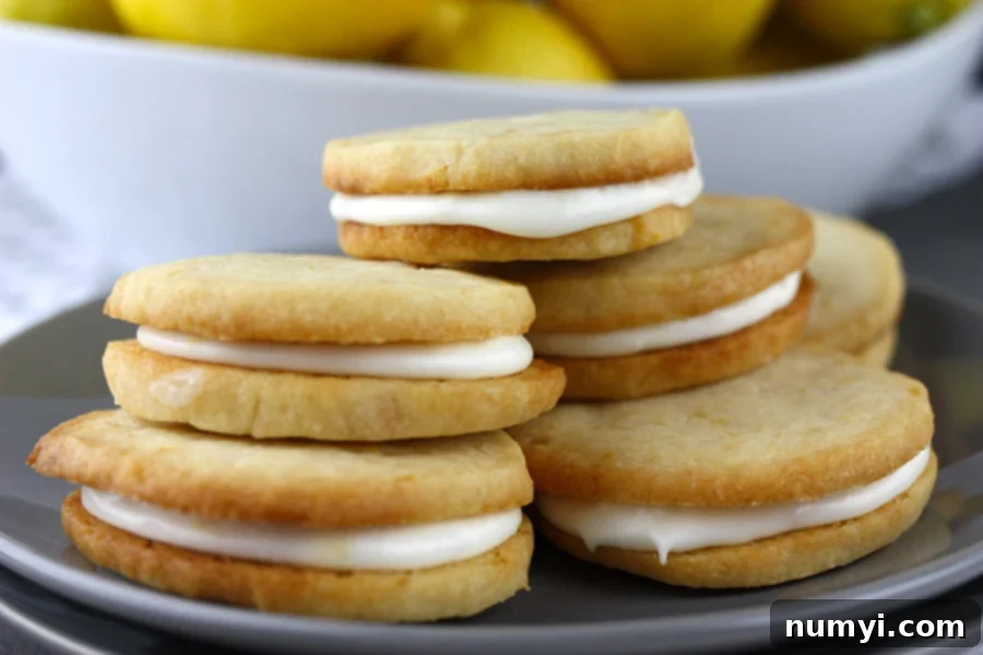 Zesty Lemon Cream Sandwiches 2 Lemon Sandwich Cookies stacked up on a plate with a bowl of fresh lemons behind them, evoking freshness and delight.