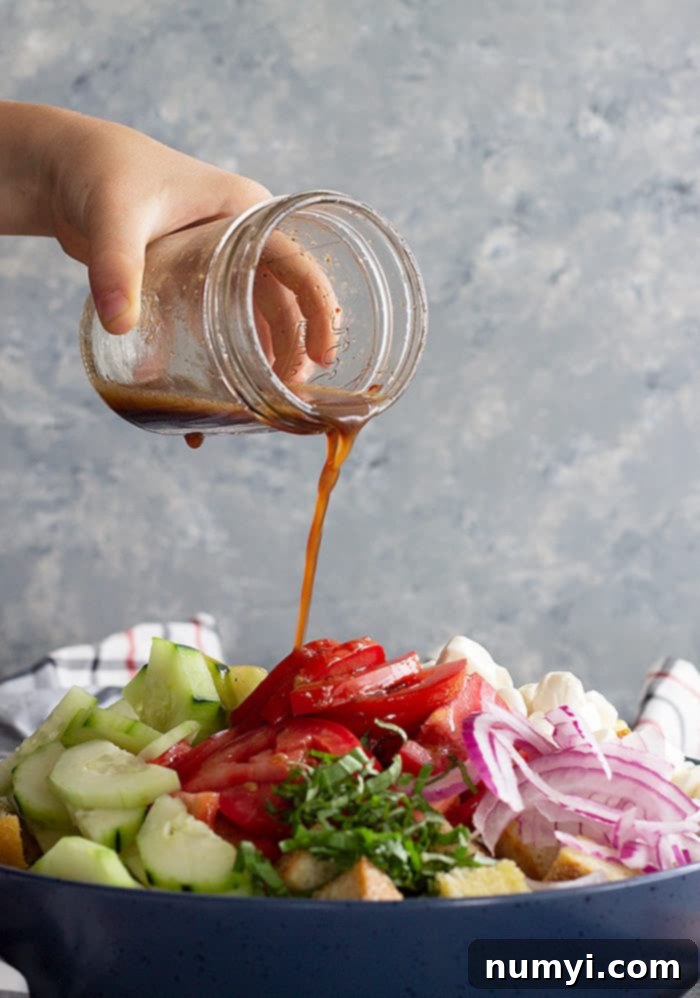 Dressing pouring over panzanella salad.