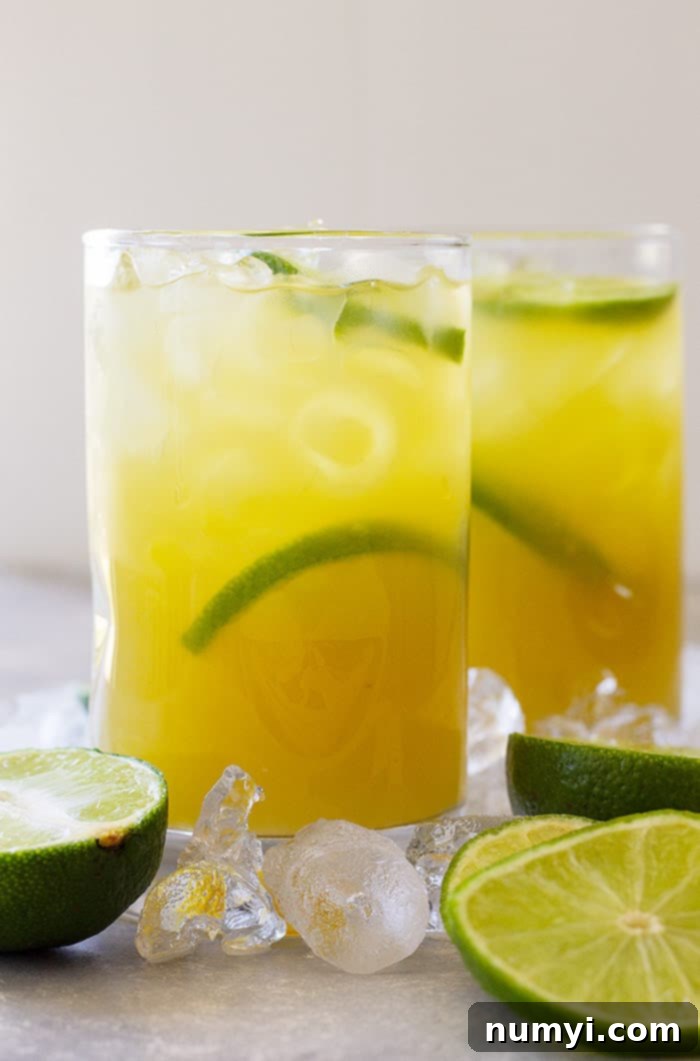 Tall glass of classic margarita with lime wedges and ice.