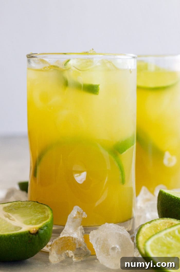 Tall glass of classic margarita with lime wedges and ice.