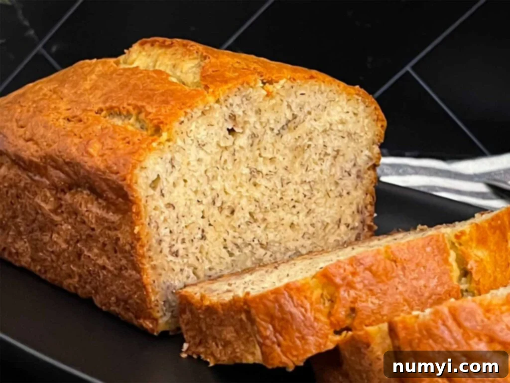 Melt-In-Your-Mouth Banana Bread Made Simple 2 Slices of banana bread and the remaining loaf on a dark plate on a dark surface, highlighting its moist texture.