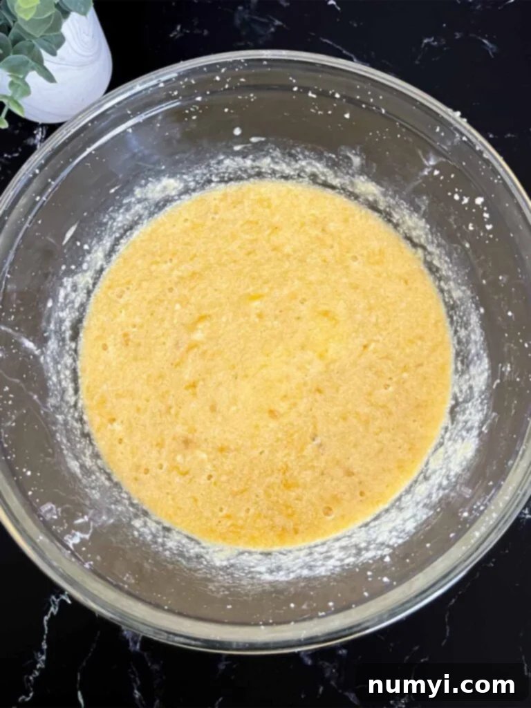 Melt-In-Your-Mouth Banana Bread Made Simple 4 Mashed bananas being incorporated into the creamy banana bread batter in a clear glass mixing bowl.