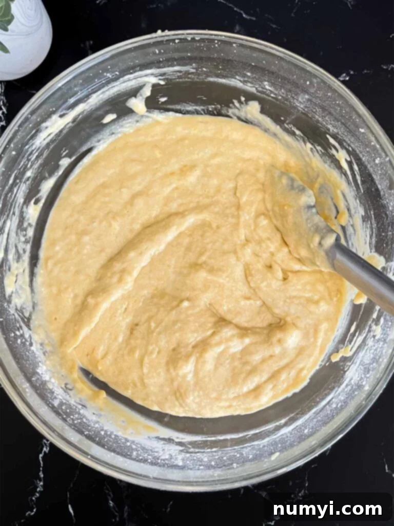 Melt-In-Your-Mouth Banana Bread Made Simple 5 Smooth banana bread batter in a clear glass mixing bowl on a dark surface, ready to be poured.