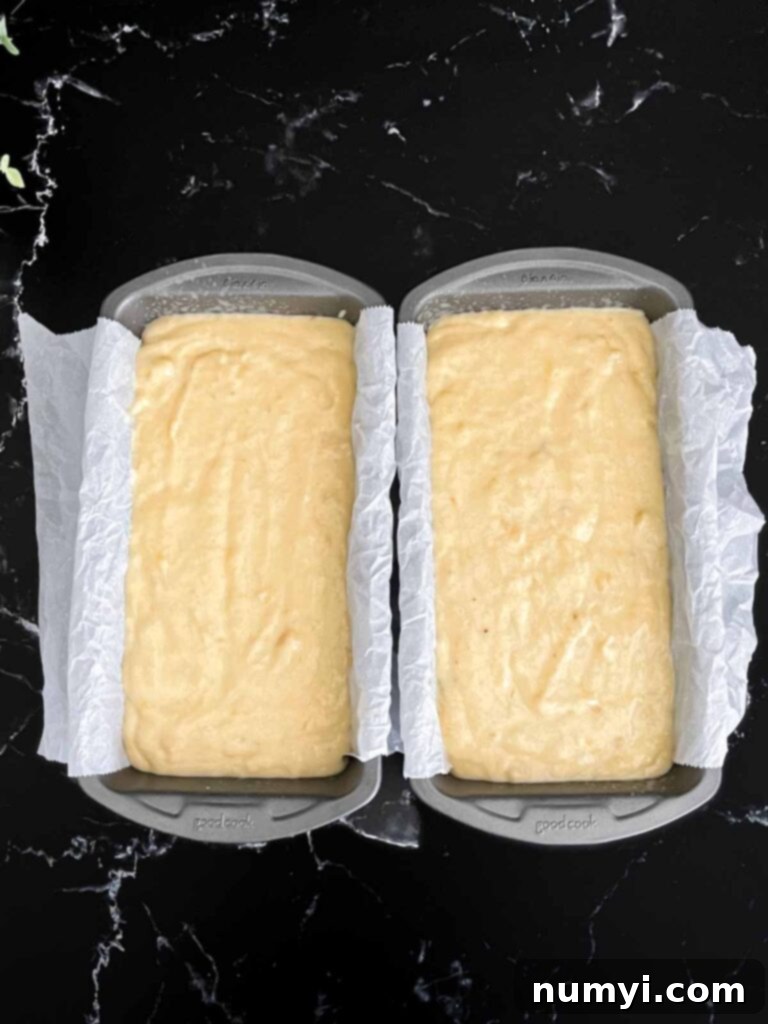 Melt-In-Your-Mouth Banana Bread Made Simple 6 Banana bread batter perfectly divided into two 8x4 loaf pans, ready for baking, lined with parchment paper slings.