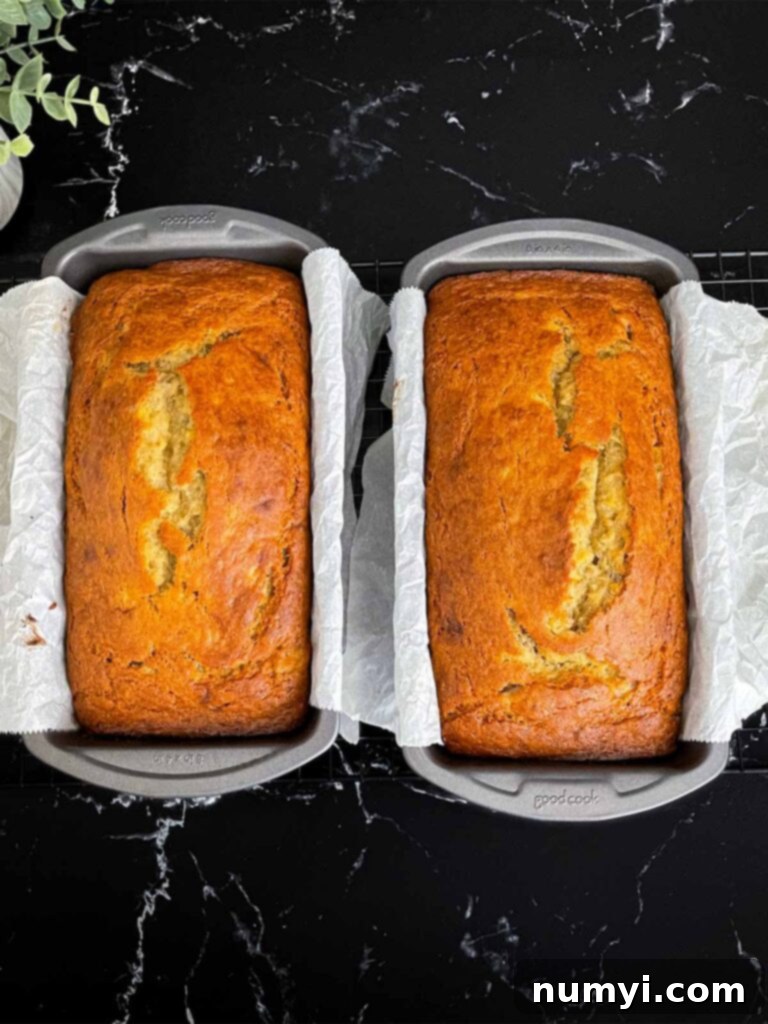 Melt-In-Your-Mouth Banana Bread Made Simple 7 Two freshly baked banana bread loaves in their 8x4 loaf pans, still lined with parchment paper, cooling.