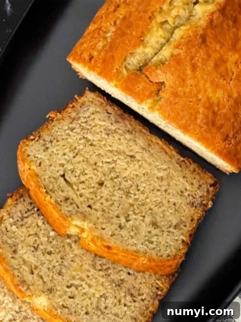 Melt-In-Your-Mouth Banana Bread Made Simple 8 Delicious slices of banana bread arranged artfully next to a whole loaf on a dark plate, showcasing its golden crust and moist interior.
