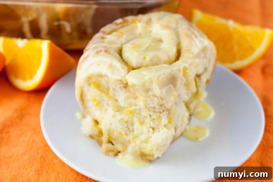 Homemade Orange Swirls in Just One Hour 2 A single homemade orange roll, perfectly golden brown and glazed, resting on a clean white plate, ready to be enjoyed.