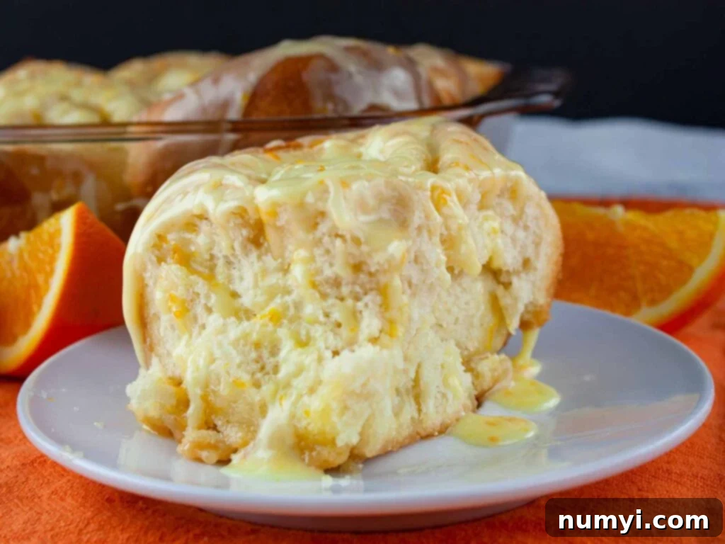 Homemade Orange Swirls in Just One Hour 3 Close-up of a warm, freshly baked orange roll with a generous citrus glaze, showing its soft, fluffy interior.