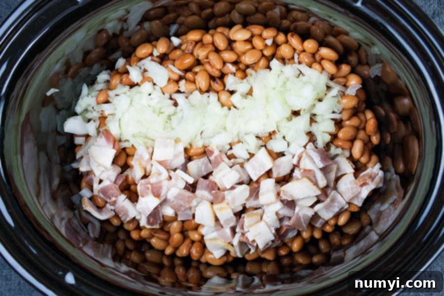 Beans, diced bacon, and diced onions in slow cooker crock before sauce is added.