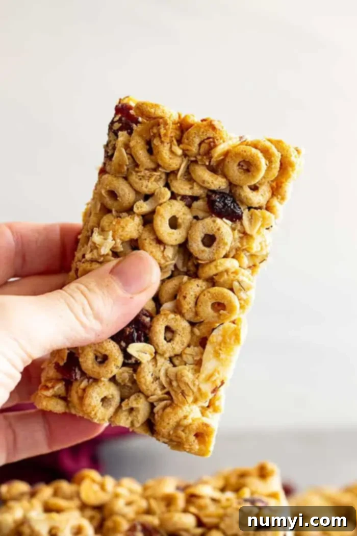 A hand holding a single Cheerio granola bar, showcasing its golden color and inviting texture.