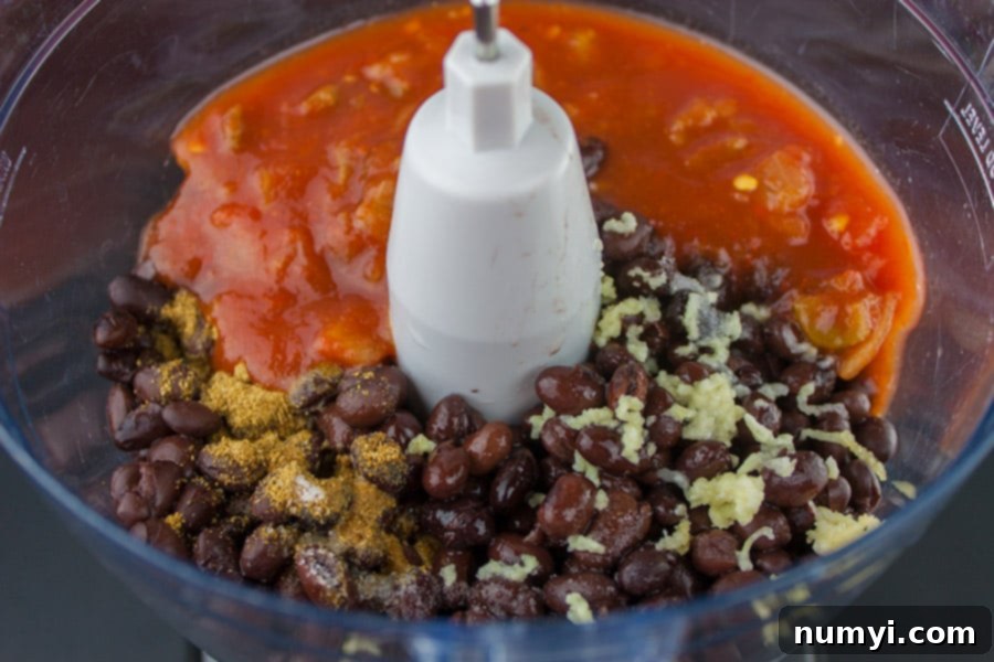All the fresh ingredients for easy black bean dip, including rinsed black beans, salsa, garlic, lime, and cumin, carefully placed in a food processor bowl before blending.